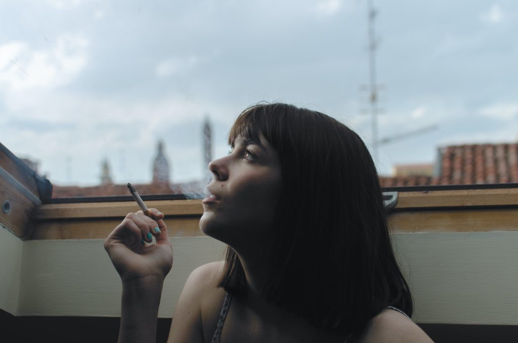 Young woman wearing tank top smoking cigarette on balcony